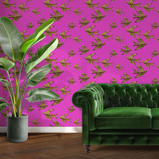 pattern of gold birds on a pink background shown as wallpaper in a room with green velvet sofa and large plant